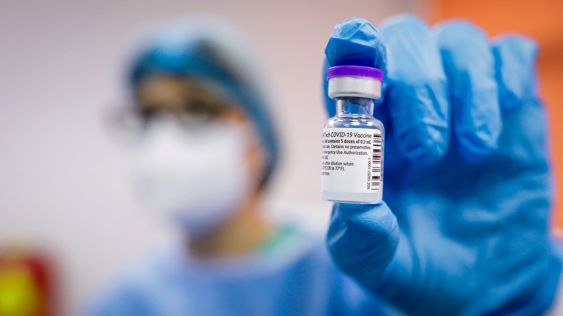 A hand in a disposable glove holds an ampoule of the COVID-19 vaccine